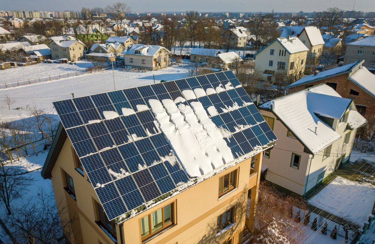 House roof covered with solar panels in winter with snow on top.